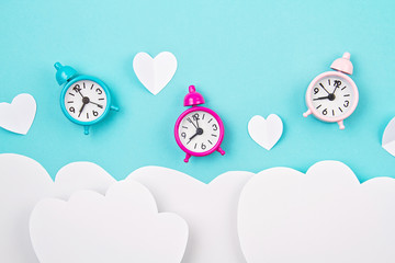 White paper hearts, alarm clocks and clouds over the tuquiose background. Sainte Valentine,...