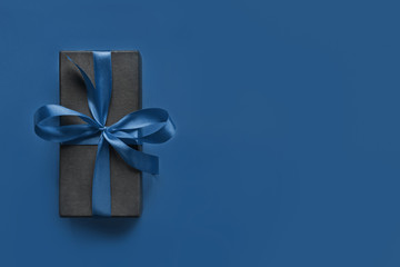 Black gift box wrapped with blue ribbon on classic blue surface.