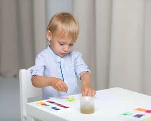 Cute little boy paints with watercolors while sitting at the tab