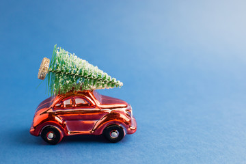 Red toy car with a christmas tree on the roof, blue trend background. Color of the year