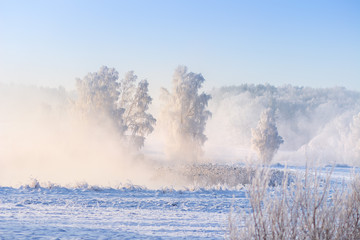 Scenic winter landscape in the foggy morning. Beautiful snowy nature at sunrise. Cold misty river in frost on clear morning. Christmas holiday background
