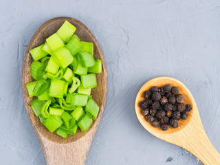 Sliced green onions and black pepper in a wooden spoons on a gray concrete background. Healthy eating concept