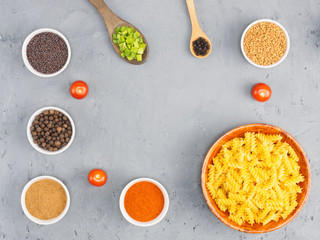 Pasta in wooden bowl, red chili pepper, small tomatoes, masala, allspice, green onion, black pepper, mustard seeds, fenugreek on a gray concrete background with copy space. Healthy eating concept