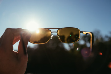 Hand holding sunglasses outdoors, blue sky, sunbeam and lens flares