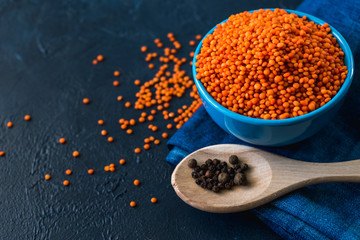Bowl with red lentil seeds in a classic blue background. Lentil seeds and pepper