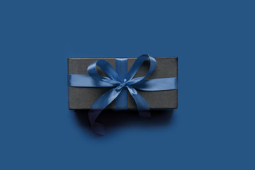 Black gift box wrapped with blue ribbon on classic blue surface.