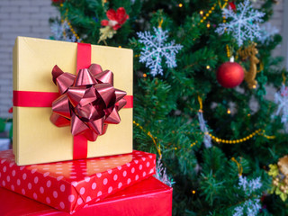Foreground gift boxes wrapped in yellow and red paper adorned with Santa Claus hats.Beautifully decorated Christmas tree to celebrate New Year and Christmas.Copy space