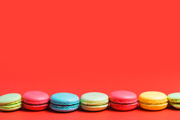 Bright red background for text with colorful yellow, green, blue, pink macaroons. Copy space for pastry chef, cafe