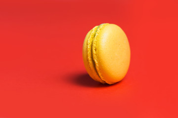 Closeup of one yellow sweet macaroon on red background. Sweet French pastries for tea