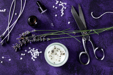 Handmade lavender scented candle with essential oil, flowers, wax, wicks, and scissors, a flat lay...