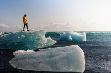 Tourist standing on an iceberg at the Diamond Beach, Iceland - Powered by Adobe