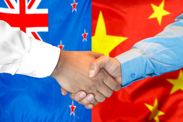 Handshake on New Zealand and China flag background.