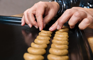 Female hands placing vanilla crescent roll cookies dough on black baking tray. Close-up of shaping traditional Czech Christmas and wedding nutty biscuits on sheet pan. Making of sweet fragrant pastry.