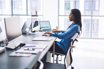 Elegant pleased ethnic woman working at computer in office