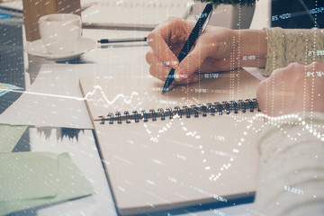 Forex chart hologram on hand taking notes background. Concept of analysis. Double exposure