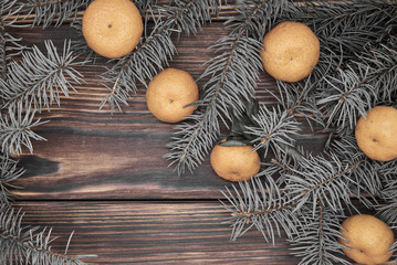 Tangerines and fir branches on a rough wooden background.