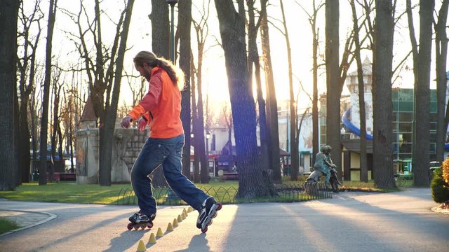 Rollers are a mans favorite hobby. A professional roller masterfully performs a difficult ride on the pavement of a city park in the sunny weather of an autumn day. Bottom-up shooting in slow motion.