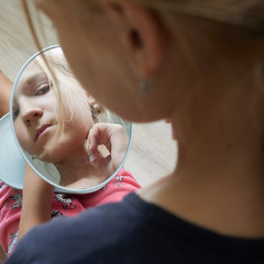 Teen or teenager girl looks at herself in mirror and looks up a pimple