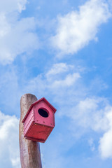 Red bird house hanging on the pole in the blue sky.
