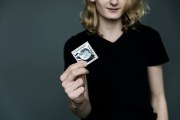 The guy holds a condom in his hand on a gray background.