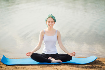 Fototapeta na wymiar beautiful young woman practices yoga near the lake