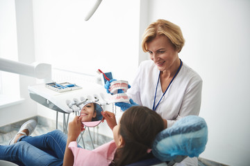Cheerful experienced dentist showing her little patient health rules