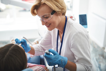 Pleasant smiling female dentist treating teeth of a little girl
