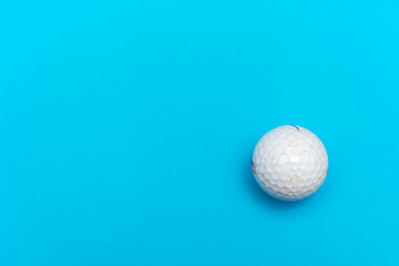 White golf a ball on a solid bright blue flat lay background symbolizing sports and activity with copy space.