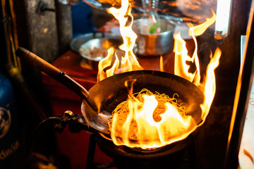 Street food chef cooking fry noodle in a black pan with fire exposure.  The traditional Thai and...