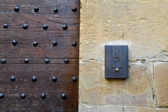 Detail of an old wood studded door with a modern doorbell for people with disabilities on a stone wall, Florence, Tuscany, Italy