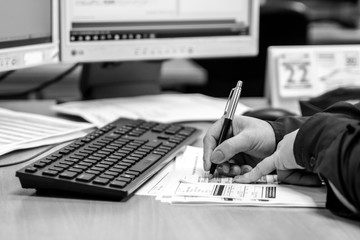 London, England, 28/01/2019 Black and White young woman working in an office doing administrative paperwork. close up of her hands writing with a pen on paper coloured fingernails and keyboard on desk