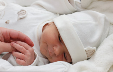 weekly baby holds hand. Baby wearing a white clotheslying. Infant just borned, have a one week.