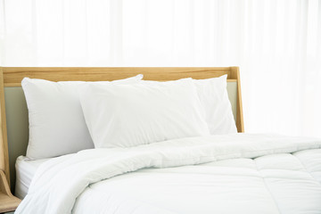 Bedroom decorated in minimal style, photograph of white pillows and wooden bed in bedroom with natural light from window.
