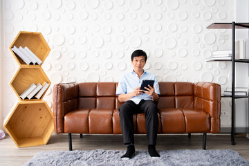 Handsome Asian elder man relaxing in living room, man using digital tablet.