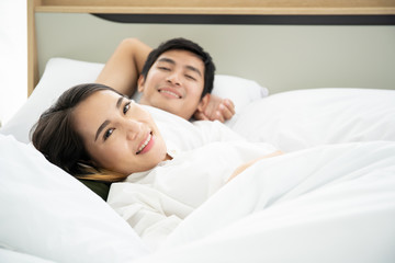Asian husband and wife relaxing on the bed together in the morning.