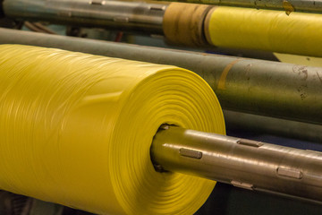 Imagery of Yellow spool of plastic packaging sheet heavy duty for industrial use outdoors. wrapped around a worn metal pole ready to feed into a machine for cutting into shape or printing logos.