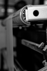 Black & White imagery of the bearing and cogs of machine feeding thin sheets of plastic packaging through a factory. sharp image of side of a machine for pressing colouring and cutting material