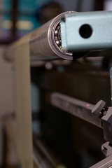 imagery of the blue bearing and cogs of machine feeding thin sheets of plastic packaging through a factory. sharp image of side of a machine for pressing colouring and cutting material