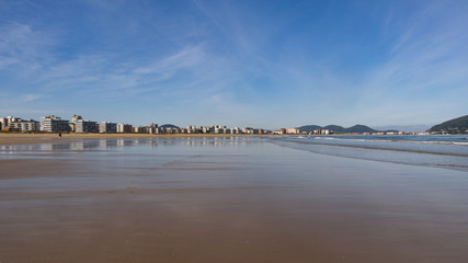 Smooth sandy beach with houses in the background on a sunny day in Laredo, Spain