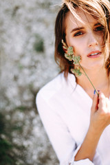 Gentle portrait of a beautiful girl or woman in a white blouse in the backlight on a sandy background