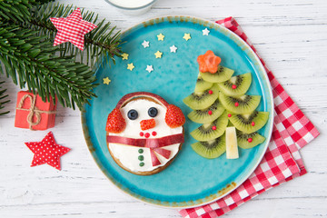 Christmas pancakes in a shape of snowman made of fresh fruits and berries and kiwi christmas tree. Glass of milk. Healthy food for kids ideas. Top view