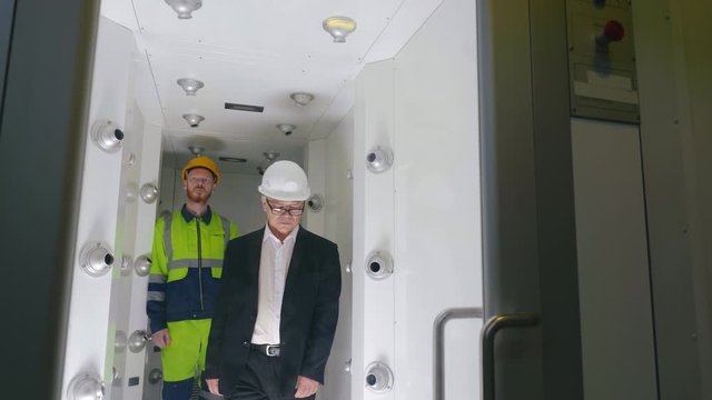 Asian engineer in formal suit and worker in uniform in air shower chamber. Remove dust and particles prepare to enter clean room. Jets blow air through filters. Scientists do protective procedures