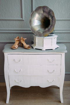 Retro photo-gramophone on a white wooden dresser, standing next to beige women's shoes with heels. Wedding theme, Studio shooting.