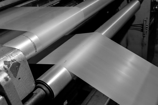 Black & White imagery of spool of plastic packaging sheet heavy duty for industrial use outdoors. wrapped around a metal pole ready to feed into a machine for cutting into shape or printing logos.