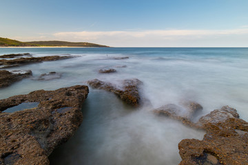 Long exposure view of water around the rock on the beach.