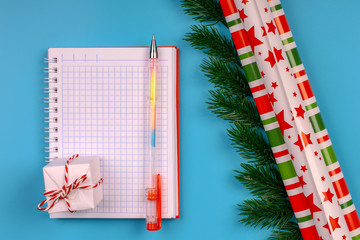 Christmas background. An open notebook for recording expenses. A pen. Packing colored paper. Fir branches. Blue background. Top view. Close-up. Place for text.