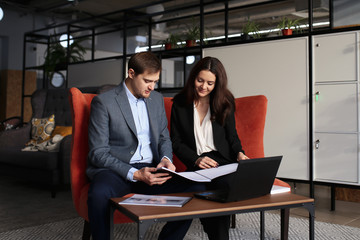 Adult serious man businessman in a business suit discussing business and work with his partner, Secretary beautiful girl and working on a laptop in a modern office.