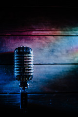 Retro microphone on wooden background and color lights with copy space for text. Vertical