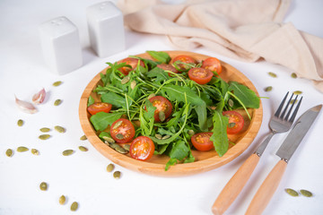 Fresh vegetable salad. Vegetarian salad of arugula, cherry tomatoes and pumpkin seeds in a wooden plate. The concept of pure and natural food. Horizontal photo.