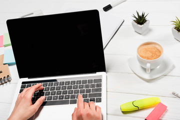 cropped view of woman using laptop at workplace with office supplies and coffee